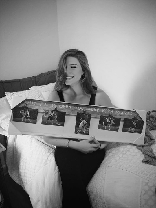 Savannah Melcher holding up the frame her parents made with them posing in Jazzercize outfits as she laughs hysterically